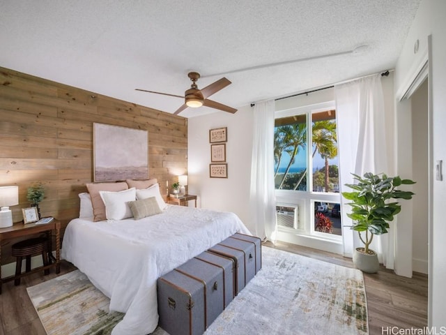 bedroom with a wall unit AC, wooden walls, wood finished floors, ceiling fan, and a textured ceiling