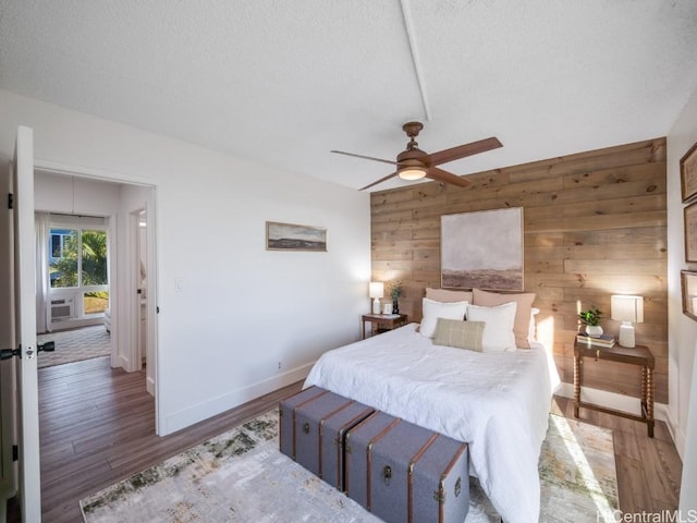 bedroom with a ceiling fan, a textured ceiling, wood finished floors, wood walls, and baseboards