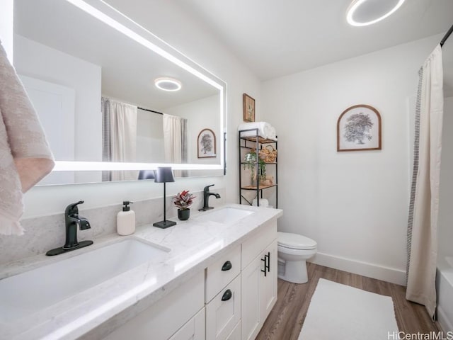 bathroom with toilet, wood finished floors, baseboards, and a sink