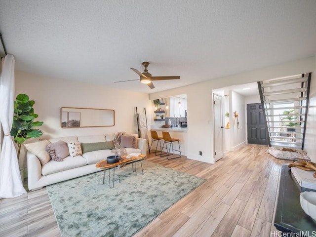 living area with baseboards, a textured ceiling, light wood-style flooring, and a ceiling fan