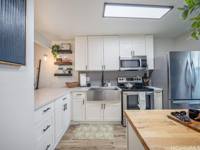 kitchen featuring open shelves, butcher block countertops, appliances with stainless steel finishes, white cabinets, and a sink