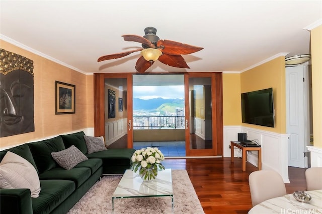 living area featuring wainscoting, a ceiling fan, wood finished floors, and crown molding