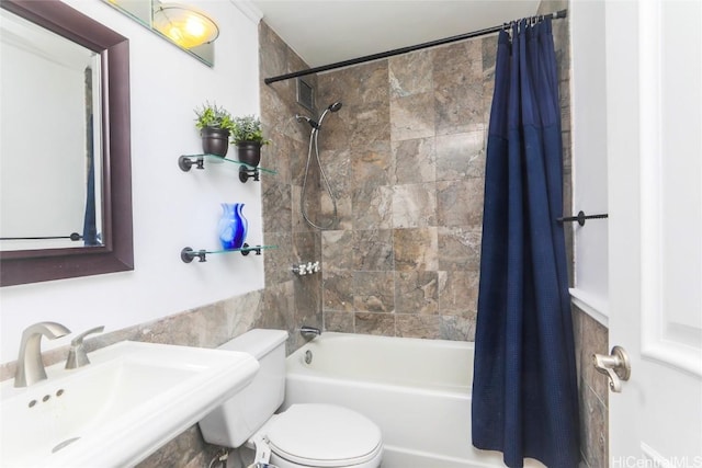 bathroom with tile walls, toilet, shower / bath combo with shower curtain, and a sink