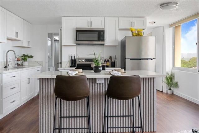 kitchen featuring a sink, a kitchen breakfast bar, dark wood finished floors, white cabinetry, and appliances with stainless steel finishes