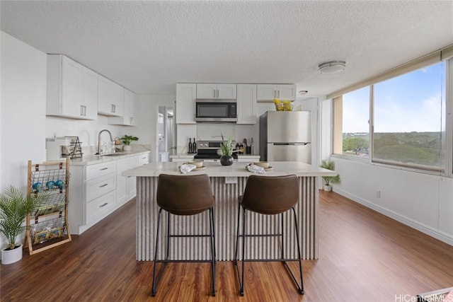 kitchen with a breakfast bar area, stainless steel appliances, dark wood-type flooring, light countertops, and white cabinetry