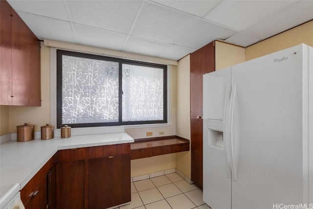 kitchen with a drop ceiling, light countertops, built in desk, and white fridge with ice dispenser