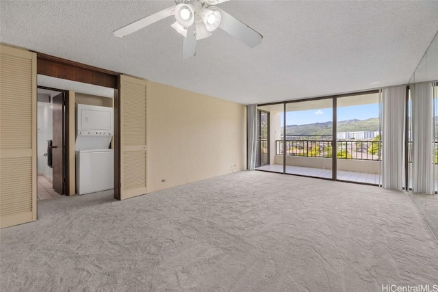 carpeted spare room with floor to ceiling windows, stacked washer and clothes dryer, a textured ceiling, and a ceiling fan