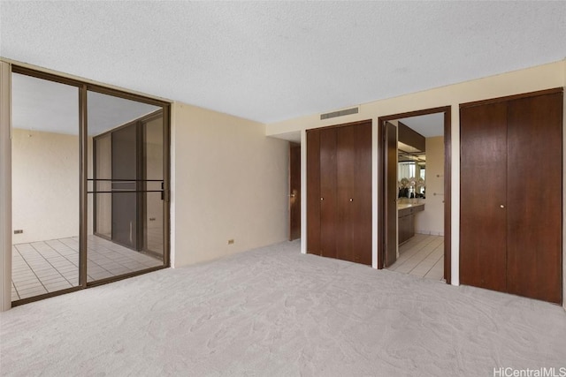 unfurnished bedroom featuring visible vents, multiple closets, carpet flooring, ensuite bathroom, and a textured ceiling