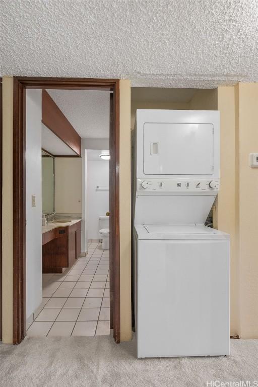 clothes washing area with light colored carpet, stacked washing maching and dryer, light tile patterned flooring, a textured ceiling, and a sink