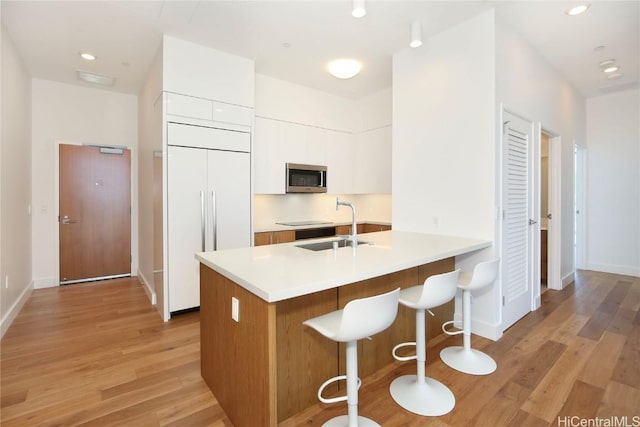 kitchen featuring stainless steel microwave, a breakfast bar, modern cabinets, paneled refrigerator, and a sink