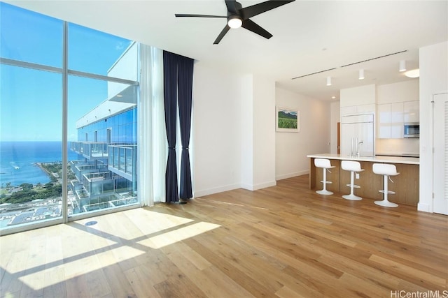 unfurnished room with a ceiling fan, baseboards, light wood-style flooring, a water view, and expansive windows