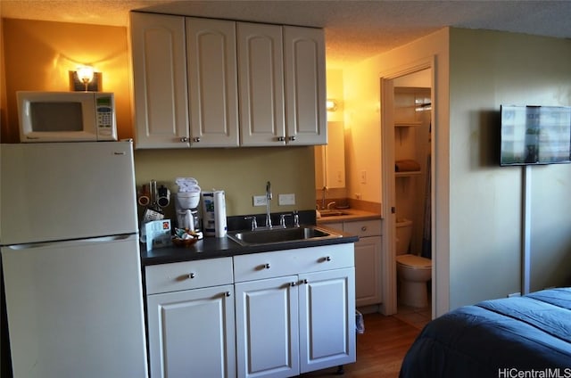 kitchen with white cabinetry, white appliances, dark countertops, and a sink