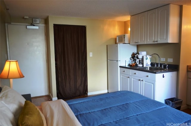 bedroom featuring baseboards, freestanding refrigerator, and a sink