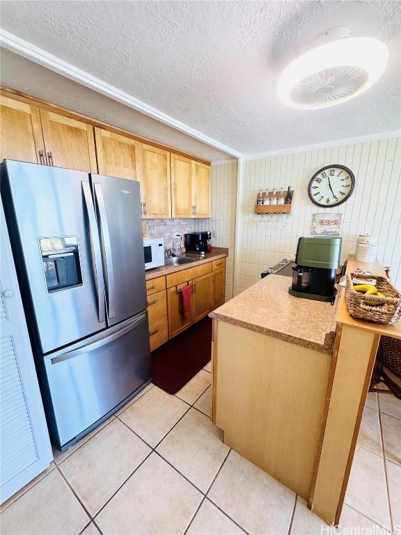 kitchen featuring white microwave, light tile patterned floors, a textured ceiling, and stainless steel refrigerator with ice dispenser