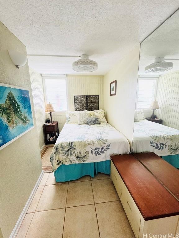 bedroom featuring multiple windows, baseboards, light tile patterned floors, and a textured ceiling