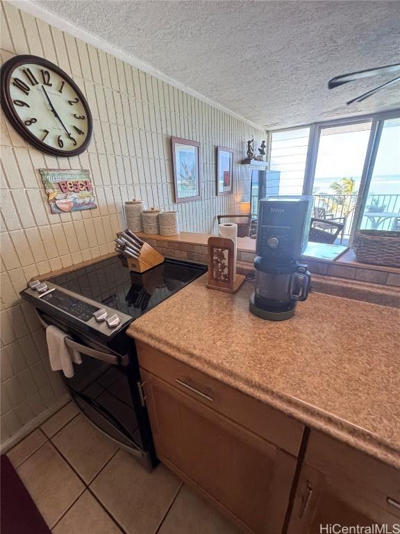 kitchen with tile patterned flooring, crown molding, black range with electric stovetop, and a textured ceiling