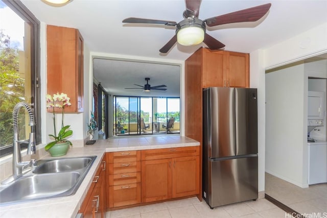 kitchen featuring a sink, brown cabinets, stacked washer and clothes dryer, and freestanding refrigerator