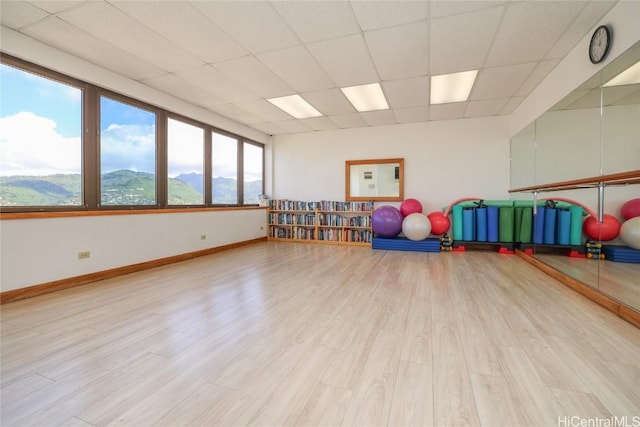 playroom featuring light wood-style flooring, a paneled ceiling, a mountain view, and baseboards