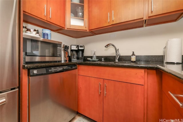 kitchen with appliances with stainless steel finishes, dark stone counters, glass insert cabinets, and a sink