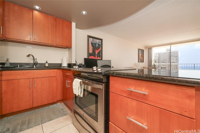 kitchen with electric stove, dark stone countertops, a sink, light tile patterned flooring, and brown cabinetry