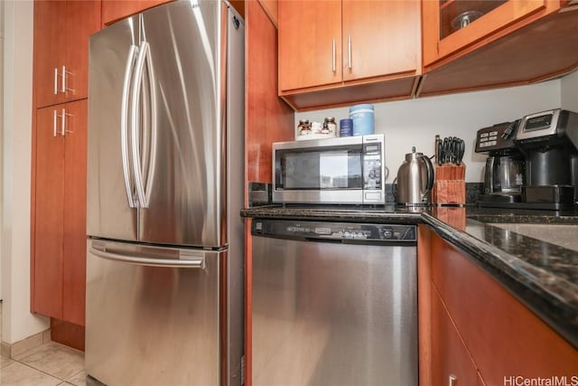 kitchen featuring stainless steel appliances, brown cabinets, light tile patterned flooring, and dark stone counters