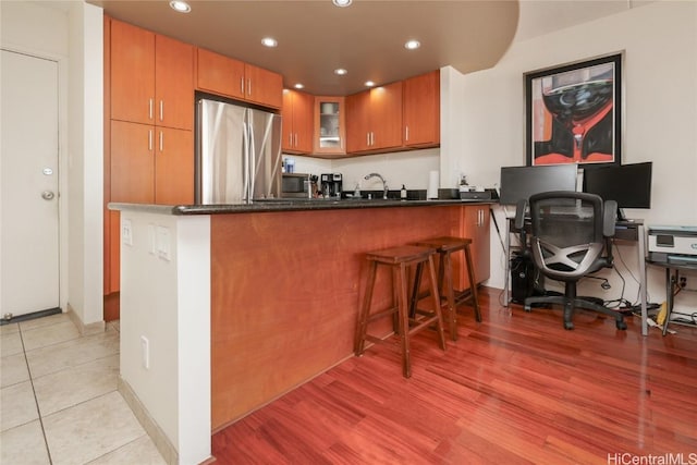 kitchen with a peninsula, light wood-style flooring, freestanding refrigerator, glass insert cabinets, and brown cabinets