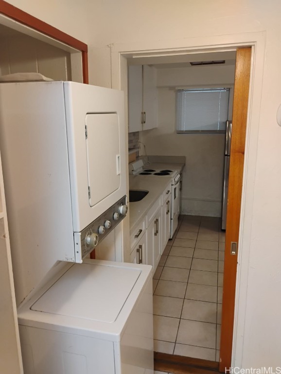 kitchen featuring light tile patterned floors, freestanding refrigerator, white cabinets, electric stove, and stacked washer and clothes dryer