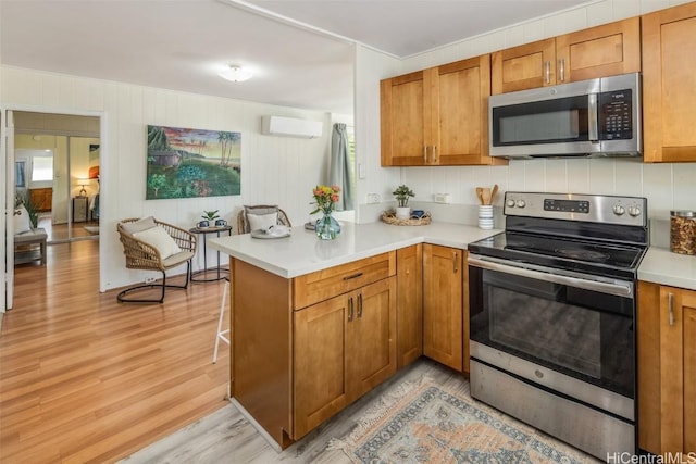 kitchen featuring brown cabinets, an AC wall unit, light wood-style flooring, appliances with stainless steel finishes, and a peninsula