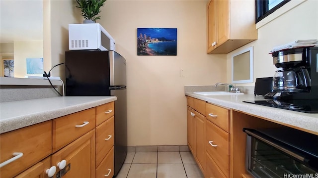 kitchen featuring light tile patterned floors, white microwave, freestanding refrigerator, a sink, and light countertops