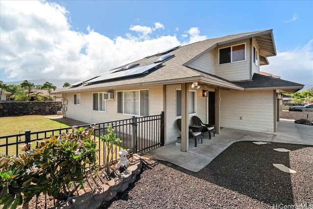view of front of home featuring a wall mounted air conditioner, a patio, roof mounted solar panels, a fenced backyard, and roof with shingles