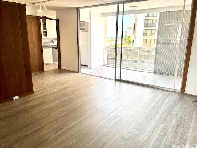 empty room with a wall of windows, rail lighting, wood finished floors, and baseboards