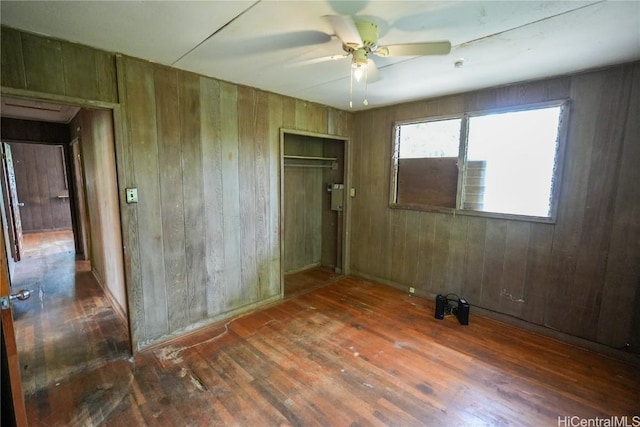 unfurnished bedroom featuring hardwood / wood-style floors, wooden walls, a ceiling fan, and a closet