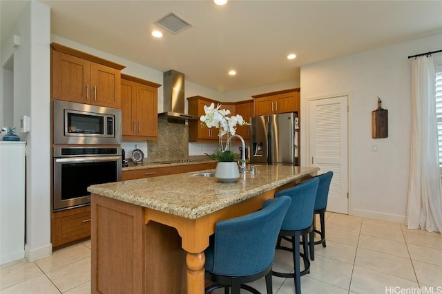 kitchen featuring visible vents, brown cabinets, a sink, stainless steel appliances, and wall chimney exhaust hood