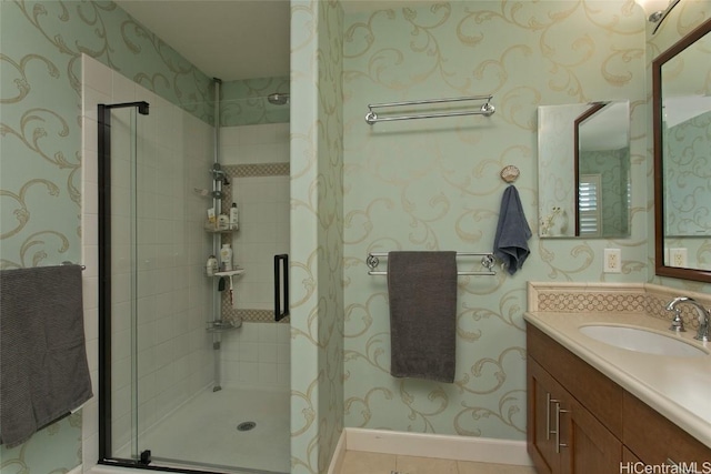 bathroom with tile patterned flooring, wallpapered walls, baseboards, a stall shower, and vanity