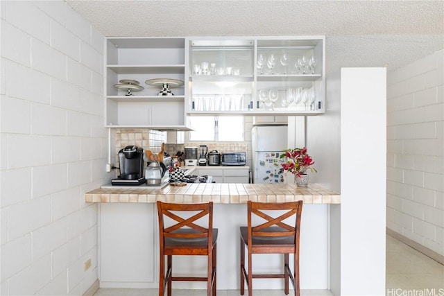 kitchen featuring white cabinetry, tile countertops, a kitchen breakfast bar, freestanding refrigerator, and a textured ceiling