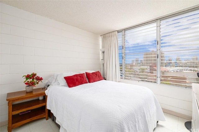 bedroom featuring a city view, concrete block wall, light tile patterned flooring, and a textured ceiling