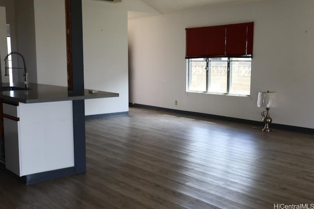 unfurnished living room with dark wood-style floors, baseboards, and a sink