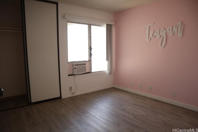 unfurnished bedroom with cooling unit, baseboards, a textured ceiling, and wood finished floors