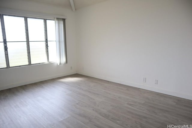 unfurnished room with lofted ceiling with beams, baseboards, and wood finished floors