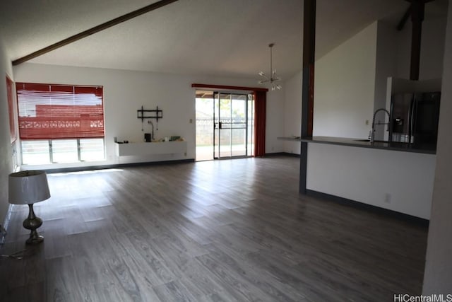 unfurnished living room featuring baseboards, wood finished floors, a notable chandelier, high vaulted ceiling, and a sink