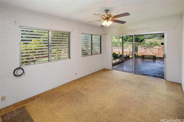 carpeted empty room with concrete block wall and ceiling fan