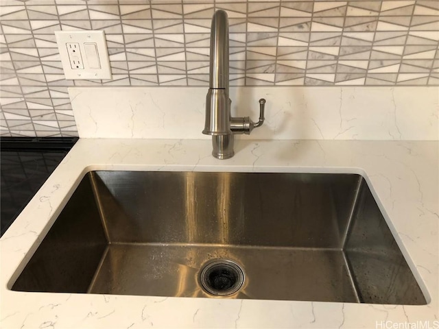 details featuring backsplash, light stone countertops, and a sink