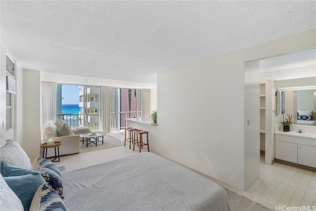 bedroom with a sink, access to exterior, a water view, and a textured ceiling