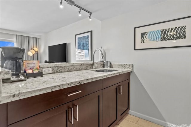 kitchen featuring light tile patterned floors, light stone countertops, baseboards, a sink, and dark brown cabinets