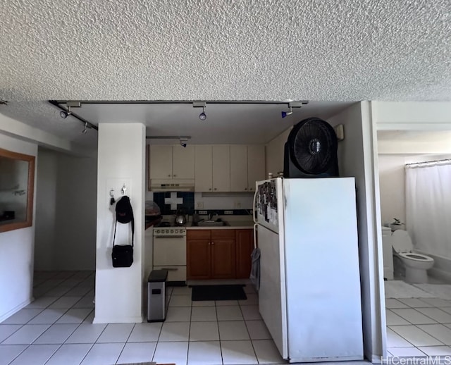 kitchen featuring under cabinet range hood, a sink, a textured ceiling, white appliances, and light tile patterned flooring