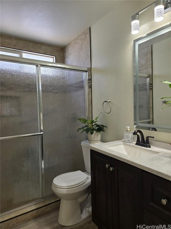 full bath featuring a shower with door, toilet, vanity, and wood finished floors