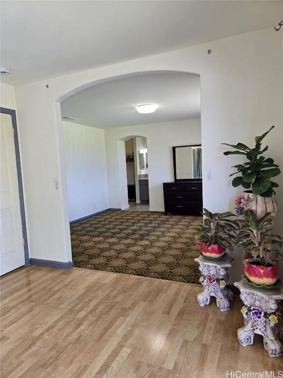 unfurnished living room featuring wood finished floors, arched walkways, and baseboards