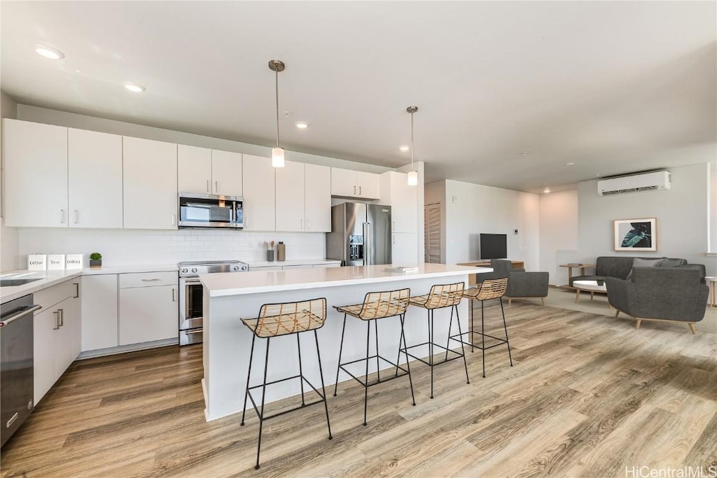 kitchen featuring light wood finished floors, a kitchen island, an AC wall unit, a kitchen bar, and appliances with stainless steel finishes