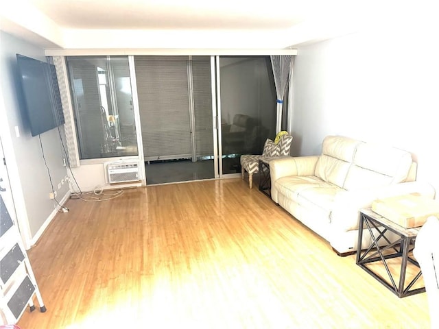 living area featuring an AC wall unit, baseboards, and wood finished floors