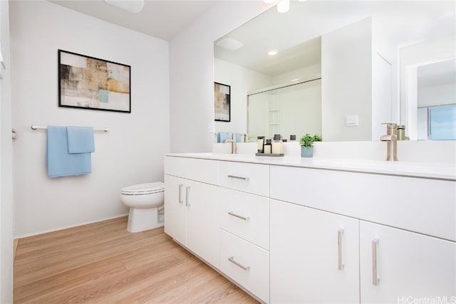 full bath featuring toilet, a stall shower, a sink, wood finished floors, and double vanity